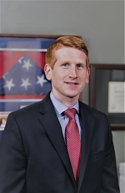 A man in suit and tie standing next to an american flag.